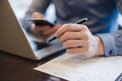 Man at desk using cell phone and holding ball pen in his hand, close-up