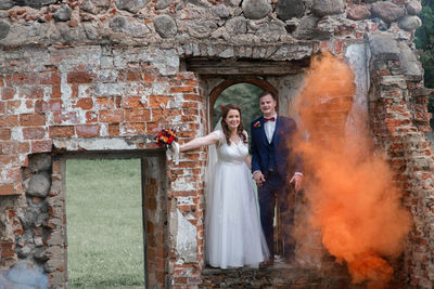 Full length of newlywed couple standing by abandoned built structure