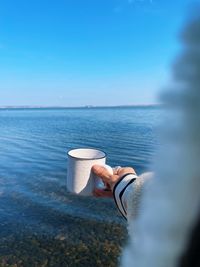 Cropped image of person pouring water against blue sky