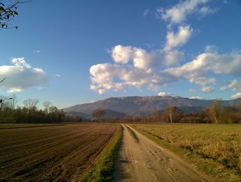 Dirt road amidst field against sky