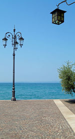 Street light by sea against clear blue sky