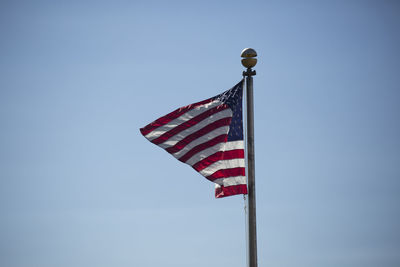 American flag waving vigorously in the wind against a blue sky