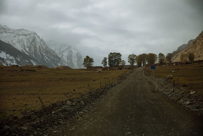 Dirt road amidst field against sky