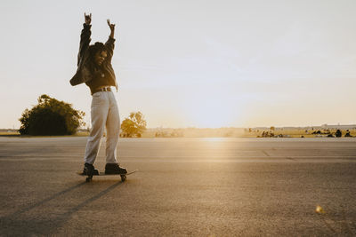 Cheerful woman with hand raised skating on road in park