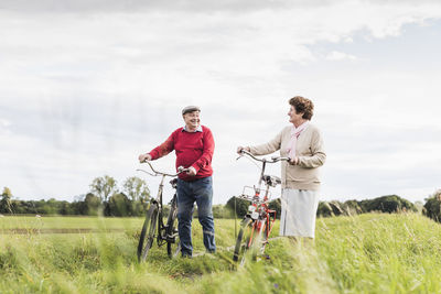 Senior couple pushing bicycles in rural landscape