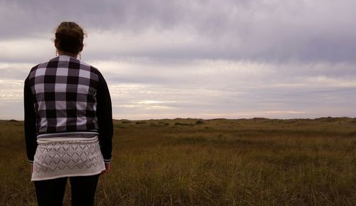 Rear view of man standing on field against cloudy sky