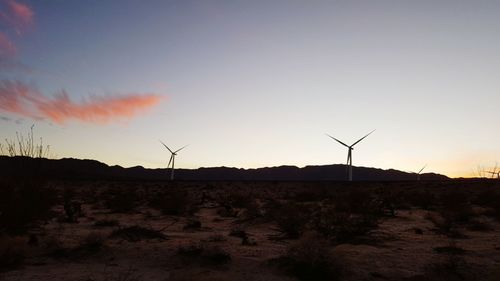 Windmills on landscape against sky at sunset