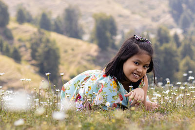 A cheerful smiling indian girl child lying on field full of calendula flowers looks at camera