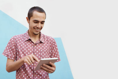 Smiling man using digital tablet against wall