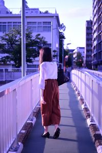 Rear view of woman walking on footbridge in city