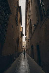 Rear view of man walking on footpath amidst buildings in city