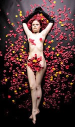 Full length of sensuous naked woman covered with rose petals while lying down on bed