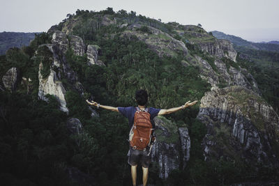 Rear view of man with arms outstretched standing at mountains 