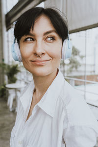 Smiling businesswoman with short hair listening music through wireless headphones