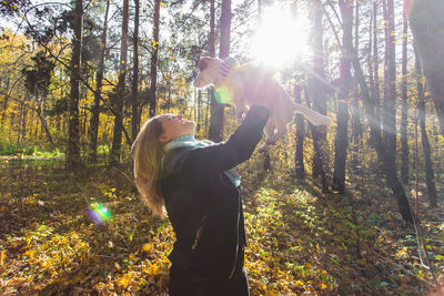 Woman photographing sun shining through trees in forest