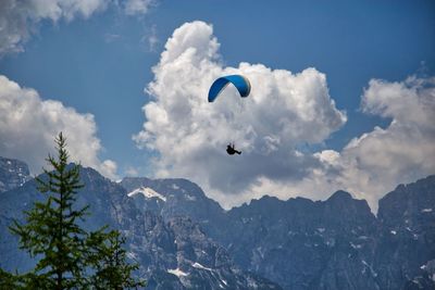 Low angle view of person paragliding over mountains against sky