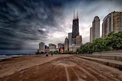 Low angle view of john hancock center seen from beach against cloudy sky