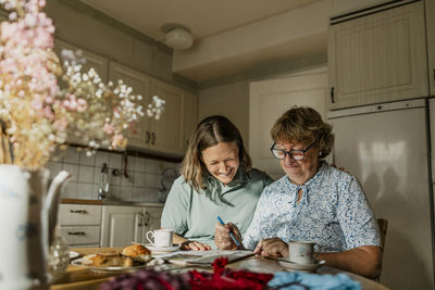 Happy senior woman and female nurse solving crossword puzzle at home