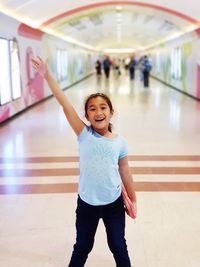 Portrait of cheerful girl with hand raised standing underground walkway