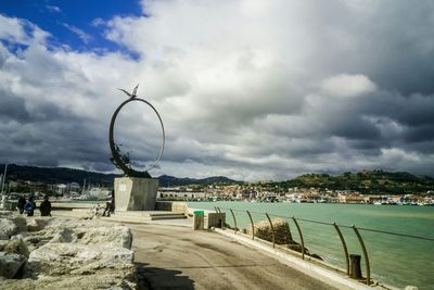 Footpath by river against cloudy sky