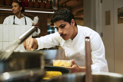 Focused male chef squeezing lemon while working with colleagues at commercial kitchen