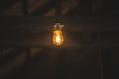 Low angle view of illuminated light bulb hanging from ceiling in darkroom