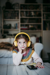 Girl wearing headphones looking away while leaning on table at home