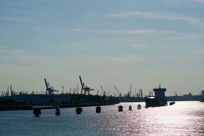 Cranes at harbor against sky