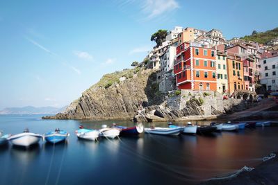 Sailboats moored on sea by buildings against sky