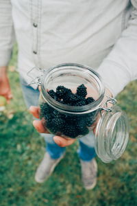 Low section of man holding blackberries in jar on field