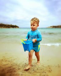 Boy standing on beach against sky