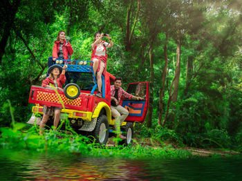 Smiling friends sitting on vehicle at forest