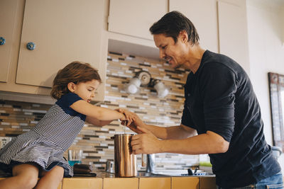 Mature father and daughter working with french press coffee maker in kitchen