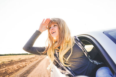 Portrait of smiling young woman in car against sky