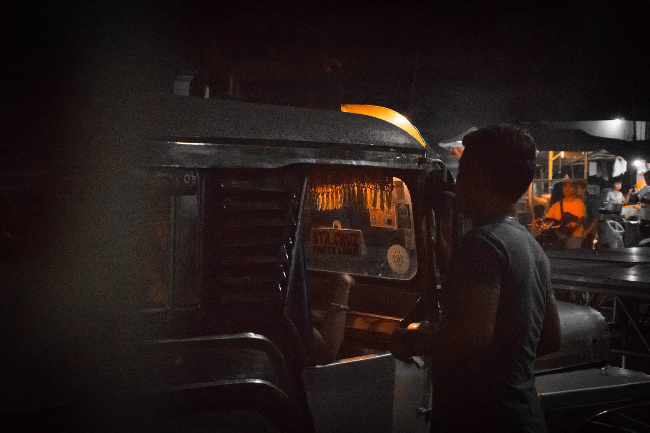 REAR VIEW OF MAN WORKING AT ILLUMINATED BUS