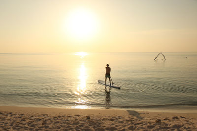 Man paddleboarding on beach against sky during sunset