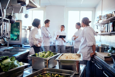 Vegetables in containers with chef team discussing in background at kitchen