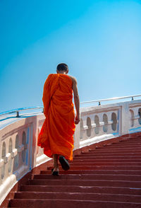 Rear view of monk standing on steps against clear blue sky