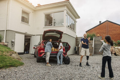 Happy family having fun while standing near electric car by house