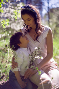 Son in a white shirt with mom stand in a blossoming apple orchard in the afternoon