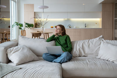 Woman freelancer sitting on couch at home working on laptop creating new ideas for working project.