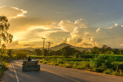 Tractor on road against cloudy sky during sunset