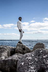 Man standing on rock by sea against sky