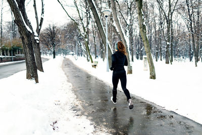 Woman running on footpath against bare trees during winter