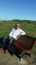 Man wearing sunglasses while sitting on bench against clear sky