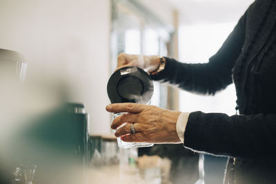 Midsection of businesswoman pouring hot water in drinking glass while standing at office