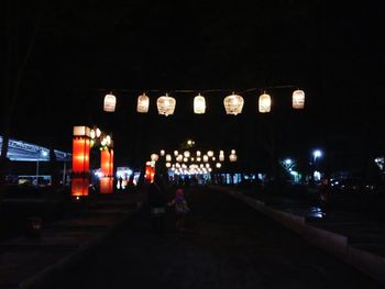 People at illuminated city against sky at night