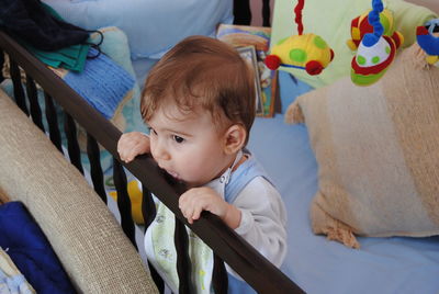 High angle view of cute baby boy standing in crib at home