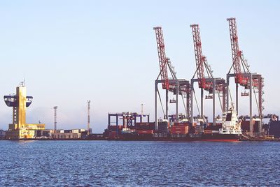 Cranes at harbor against clear sky