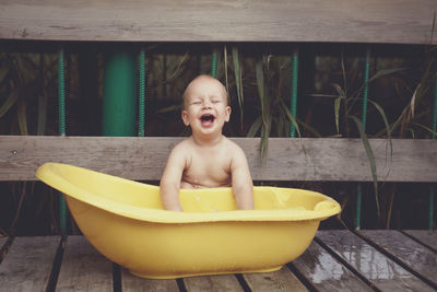 Shirtless cute baby boy playing with water in bathtub while sitting outdoors